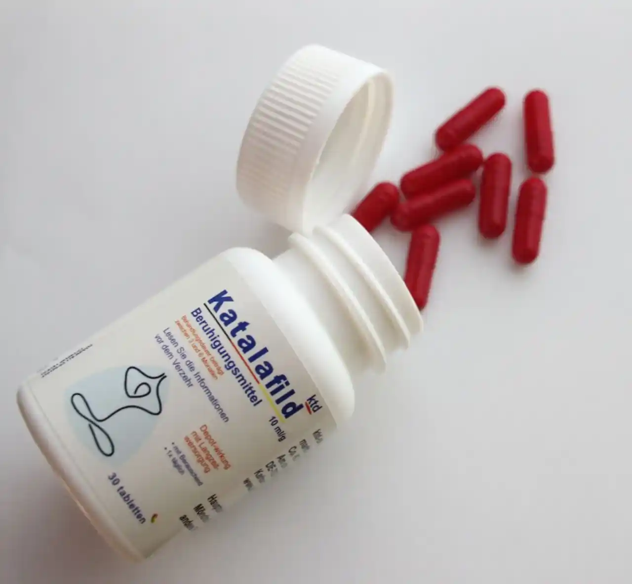 دوز 10 میلی گرم کاتالافیلد با درب باز شده و کپسول های قرمز رنگ روی سطح کاغذی سفید